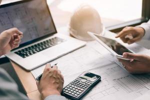Two engineering working together and using digital tablet looking blueprint and analysis with architectural plan on desk. photo