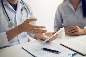 Asian doctor talking the patient at clinic while using the tablet explaining the patient condition and the treatment result. photo