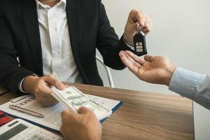 los compradores de autos nuevos y los agentes de ventas de autos están intercambiando dinero en efectivo y llaves de autos nuevos entre sí en la oficina. foto