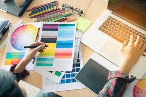 Top view of hand designer choosing colors for doing graphic on laptop. photo