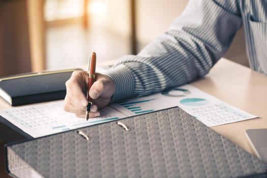 Businessman writing make note on paperwork chart summary report graph on desk for analyze data. photo