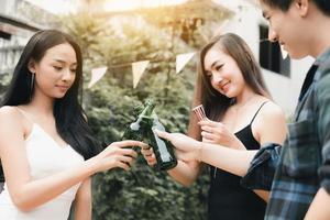 Close up of asian group enjoying toasting drinks party with clinking beer bottle. photo