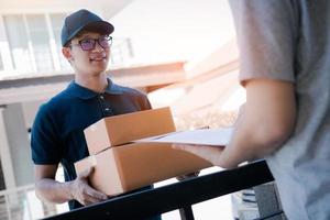 Asian cargo carrier holds a cardboard box with the package inside and the recipient is signing the package. photo