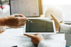 Two engineering working together and using digital tablet looking blueprint and analysis with architectural plan on desk. photo