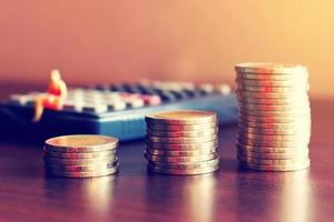 Saving finance concept, coin stack on table and miniature people sitting on calculator with background. photo