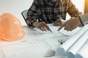 Two architect hands holding pencils pointing building blueprints in modern office. photo