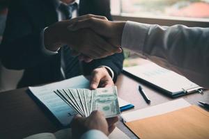 Two corporate businessmen shaking hands while one man giving money and receive cash dirty in office room with corruption concept. photo