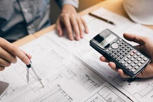 Two architect working at construction site and compass drawing pointing on blueprint with calculator calculate. photo