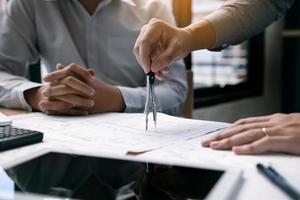 dos ingenieros trabajando juntos y usando una tableta digital buscando planos y análisis con un plan arquitectónico en el escritorio. foto