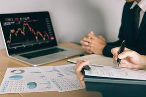 Two investors are working together with analyzing the stock data graphs in the paper and viewing the data on the laptop screen. photo