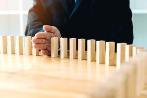 Close up hand businessman stopping wooden block from falling in the line of domino with risk concept. photo