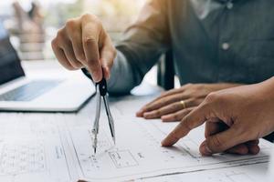 Architect working on blueprint in workplace with partnership and drawing compass. photo