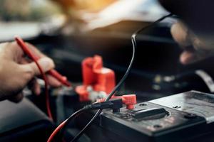 Car mechanic is using the car battery meter to measure various values and analyze it. photo