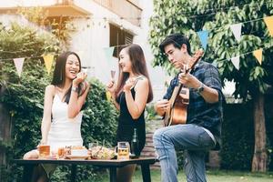 Women enjoying drinks party with guy playing guitar singing at home garden outdoors. photo