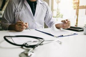 Doctor hand holding pen writing patient history list on note pad and talking to the patient about medication and treatment. photo