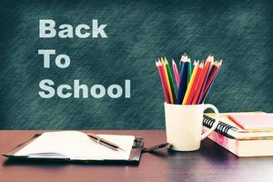 Back to school concept with books and color pencil on wooden table and written on blackboard. photo