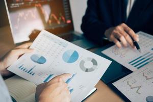 Two investors are working together with analyzing the stock data graphs in the paper and viewing the data on the laptop screen. photo