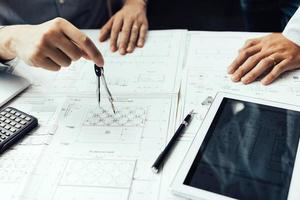 Two engineering working together and using digital tablet looking blueprint and analysis with architectural plan on desk. photo