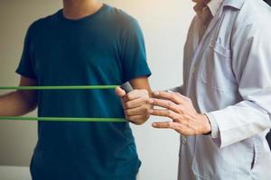 Patient doing stretching exercise with a flexible exercise band and a physical therapist hand to help in clinic room. photo