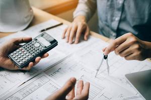 Two architect working at construction site and compass drawing pointing on blueprint with calculator calculate. photo