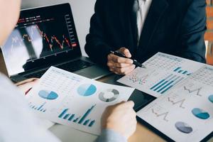 Two investors are working together with analyzing the stock data graphs in the paper and viewing the data on the laptop screen. photo