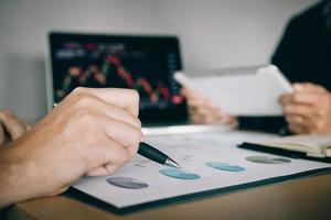 Two investors are working together with analyzing the stock data graphs in the paper and viewing the data on the laptop screen. photo