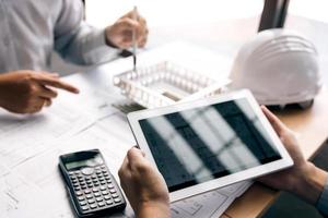 Two engineering working together and using digital tablet looking blueprint and analysis with architectural plan on desk. photo