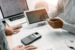 Two engineering working together and using digital tablet looking blueprint and analysis with architectural plan on desk. photo