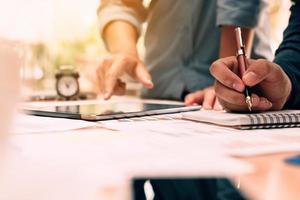Close up hand man writing make note on notebook and hand pointing with using tablet on desk in office room. photo
