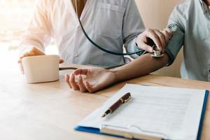 médico revisando la presión arterial de un paciente mayor en la sala de la oficina. foto