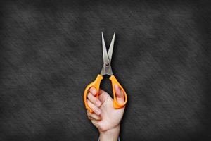 Hand is holding orange scissors on blackboard background.