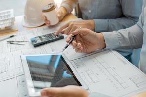 Two engineering working together and using digital tablet looking blueprint and analysis with architectural plan on desk. photo
