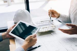 Two engineering working together and using digital tablet looking blueprint and analysis with architectural plan on desk. photo