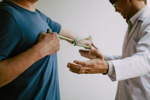 Asian male physical therapist descent working and helping to protect the hands of patients with patient doing stretching exercise with a flexible exercise band in clinic room. photo
