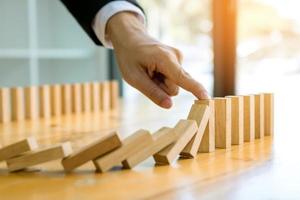 Close up finger businessman stopping wooden block from falling in the line of domino with risk concept. photo