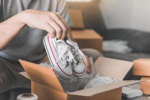un adolescente empresario asiático lleva zapatos de bebé y los pone en una caja de cartón al cliente para entregar el producto en casa. foto