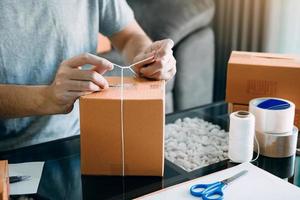 Asian young teenager owener of small business packing product in boxes preparing it for delivery. photo