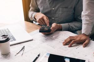 Two engineering working together and using digital tablet looking blueprint and analysis with architectural plan on desk. photo