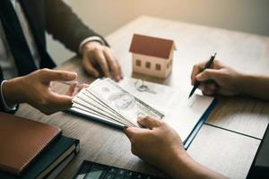 los inversores están usando un bolígrafo en el papel del contrato sobre la compra de una nueva casa mientras presentan efectivo como depósito para el agente. foto