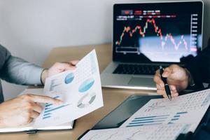 Two investors are working together with analyzing the stock data graphs in the paper and viewing the data on the laptop screen. photo