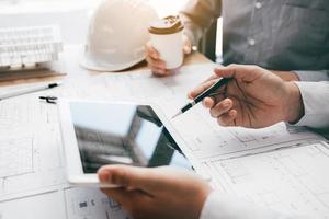 Two engineering working together and using digital tablet looking blueprint and analysis with architectural plan on desk. photo