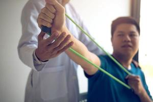 cierre el paciente de la mano haciendo ejercicio de estiramiento con una banda de ejercicio flexible y una mano de fisioterapeuta para ayudar en la sala de la clínica. foto