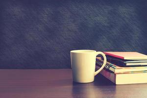 taza de café y cuaderno en la mesa de madera con fondo de tablero. foto