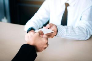 manos de dos empresarios sentados en la oficina dando y tomando tarjetas de visita vacías. foto