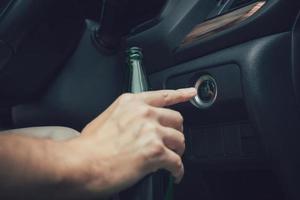 The man hand is holding a beer bottle and pressing the engine start button. photo