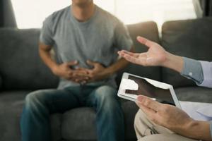 Doctor visited the patient while using tablet explaining about the patient stomach pain in the living room at home. photo