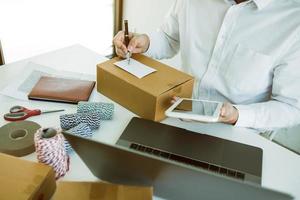 Asian business teenager is looking on tablet and writing a customer address contact to deliver the package to the customer at the destination. photo