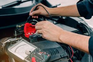 Car mechanic is using the car battery meter to measure various values and analyze it. photo