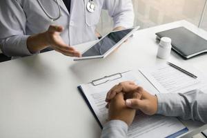 Asian doctor talking the patient at clinic while using the tablet explaining the patient condition and the treatment result. photo