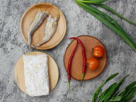 salted fish, raw tempeh and vegetables on a wooden cutting board photo